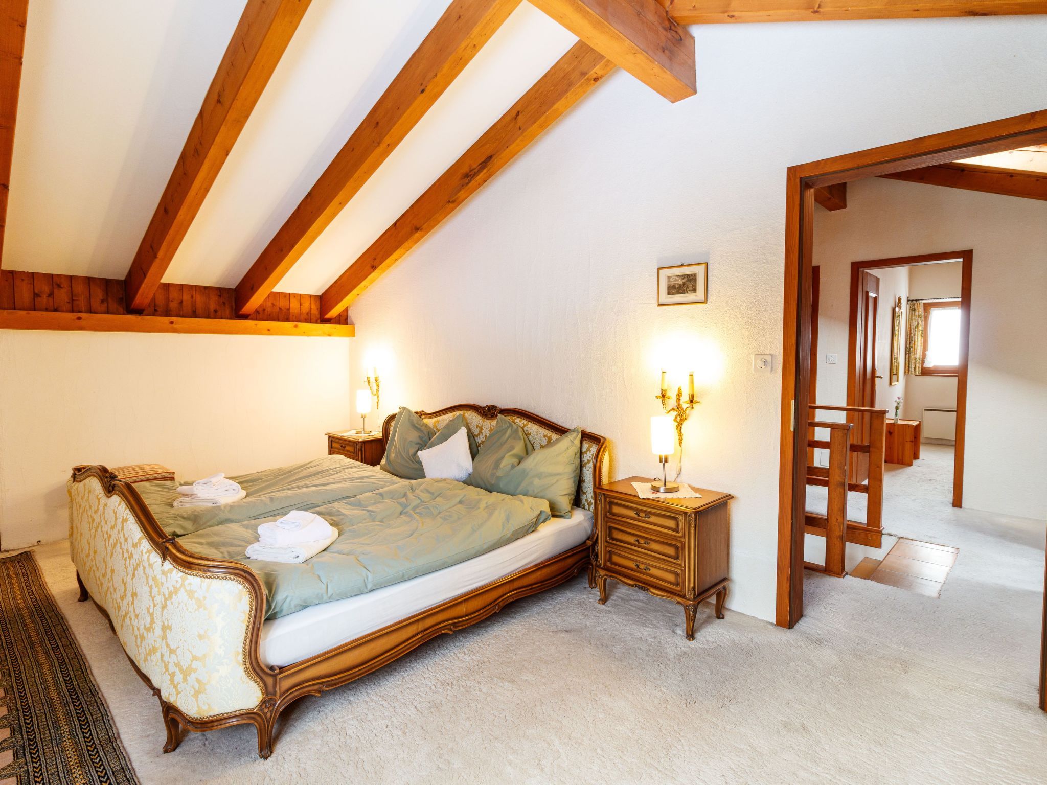 Un dormitorio con una cama grande, vigas de madera, una mesita de noche y un aparador.
