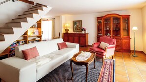 A living room with a white sofa, a red armchair, a wooden cabinet, and a staircase. - Ferienhaus Grundschera, (Brail) by Interhome (Brail)