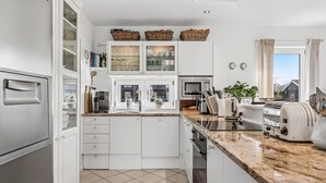 A modern kitchen with white cabinetry, a marble countertop, a built-in oven, and a window with curtains. - Nice home in Juelsminde with harbor view (Juelsminde)
