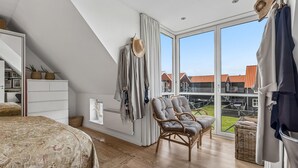 A bedroom with a sloped ceiling, large windows, a bed, a chair, and a wardrobe. - Nice home in Juelsminde with harbor view (Juelsminde)