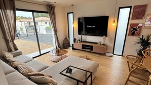 Uma sala de estar moderna com uma televisão de tela plana grande, um sofá, uma mesa de centro e um espaço de jantar com uma cadeira.