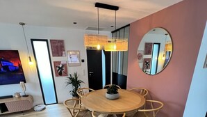 Uma sala de estar moderna com uma mesa de jantar redonda de madeira, rodeada por cadeiras, uma televisão de tela plana e um espelho grande na parede.