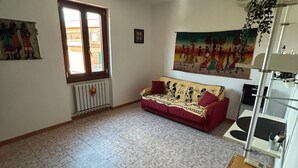 Ein Wohnzimmer mit einem roten Sofa, einer Heizung, einem Fenster und einem Bild an der Wand.