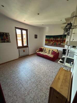 A living room with a red sofa, a radiator, a window, and a painting on the wall. - ROMAN REFLECTIONS (Roma)