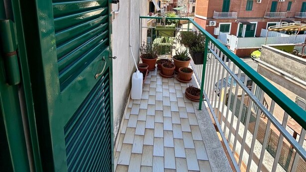 Ein Balkon mit Fliesenboden, Blumentöpfen und einem grünen Geländer.