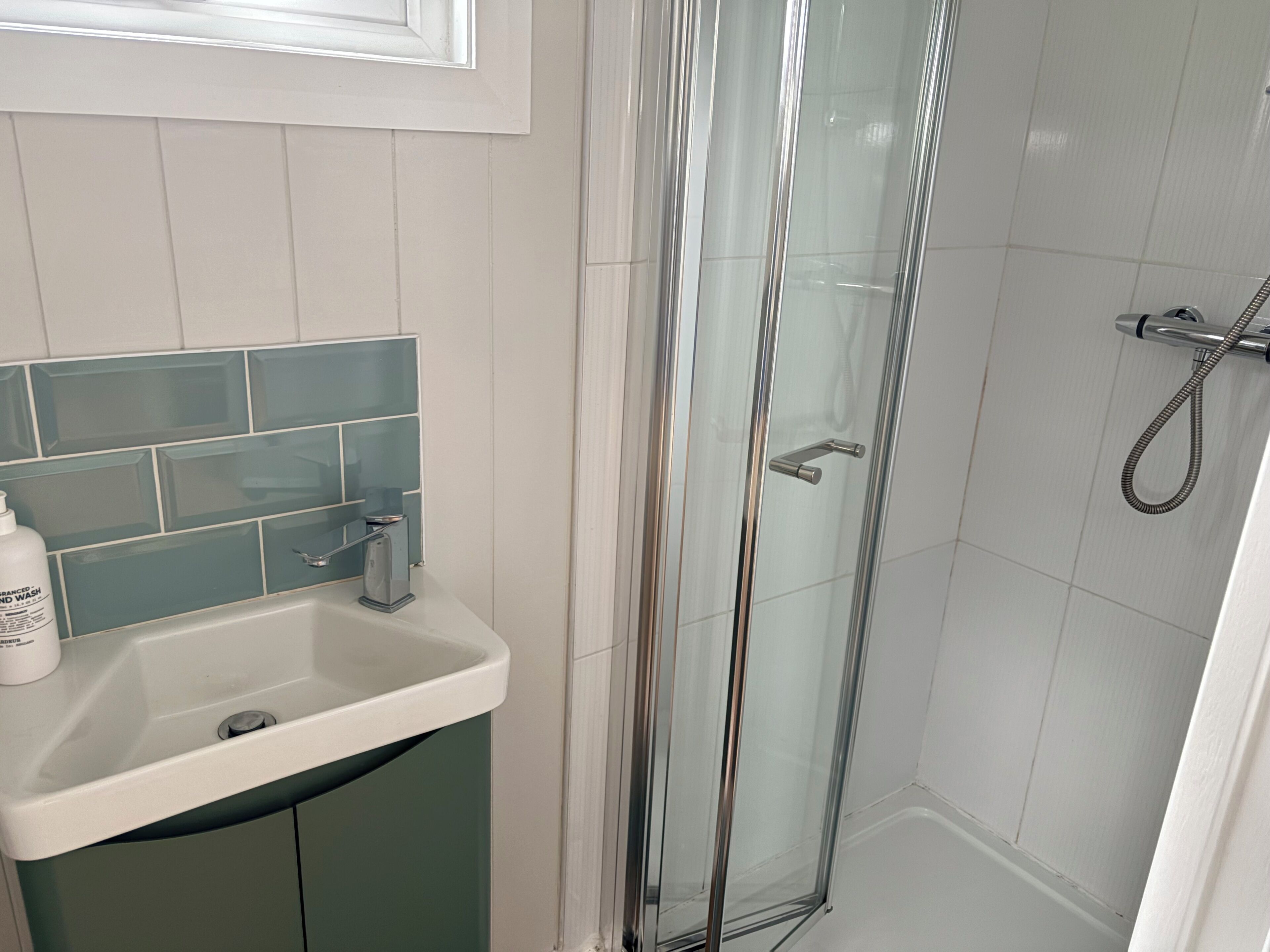 A bathroom with a glass-enclosed shower, a sink with a soap dispenser, and a tiled backsplash.