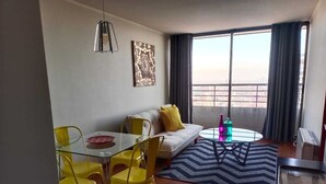 Ett modernt vardagsrum med en soffa, gula fåtöljer, ett glasbord, ett soffbord och ett stort fönster med gardiner.