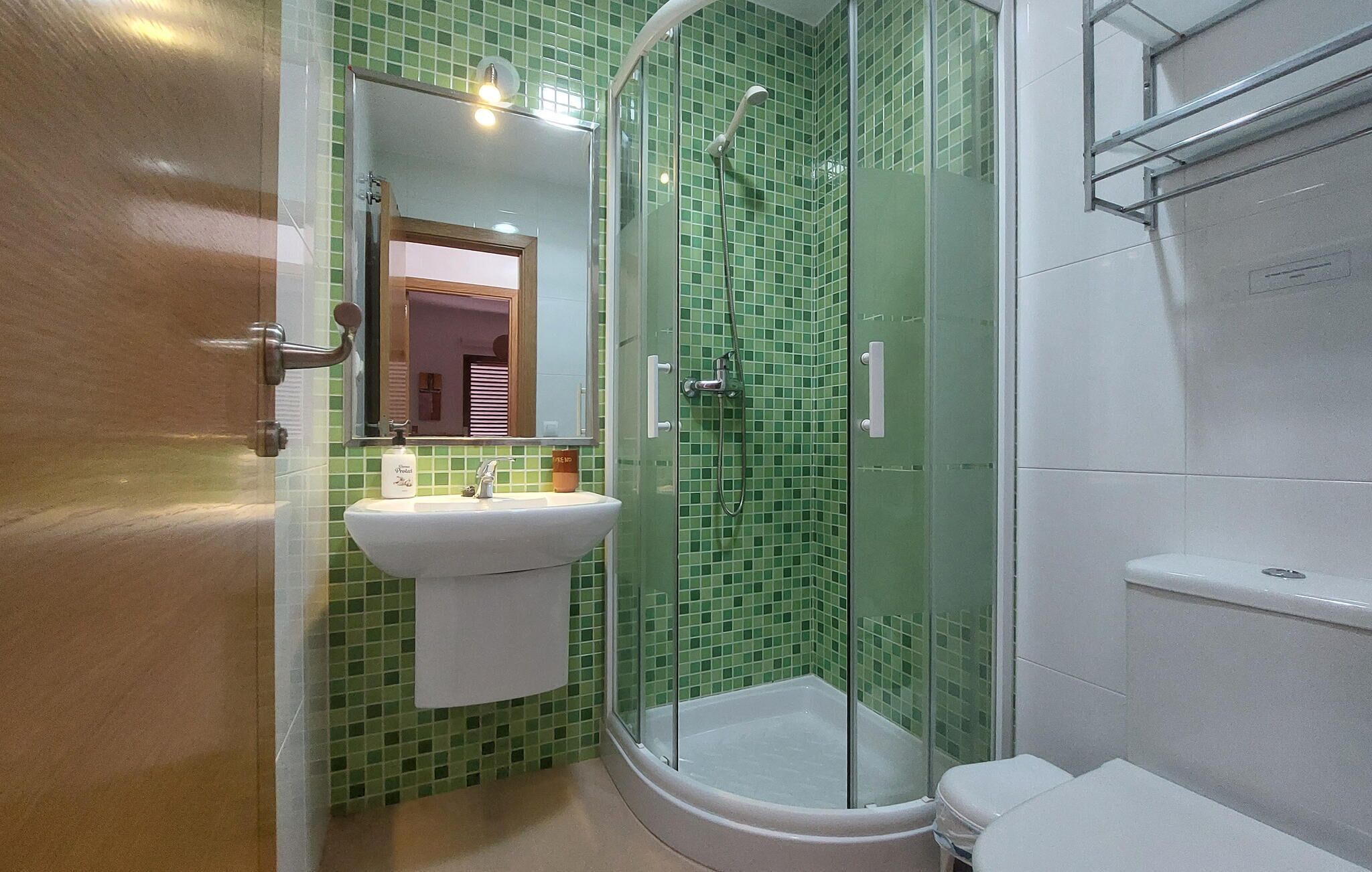 Et badeværelse med en grøn fliset bruser, en hvid vask og et toilet.