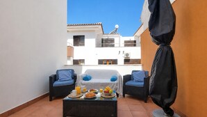 Un balcon avec deux fauteuils en osier, une table où est servi le petit-déjeuner et une vue sur les immeubles.