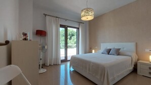Une chambre à coucher avec un grand lit, une table de chevet, une commode, une lampe sur pied et une fenêtre avec des rideaux.
