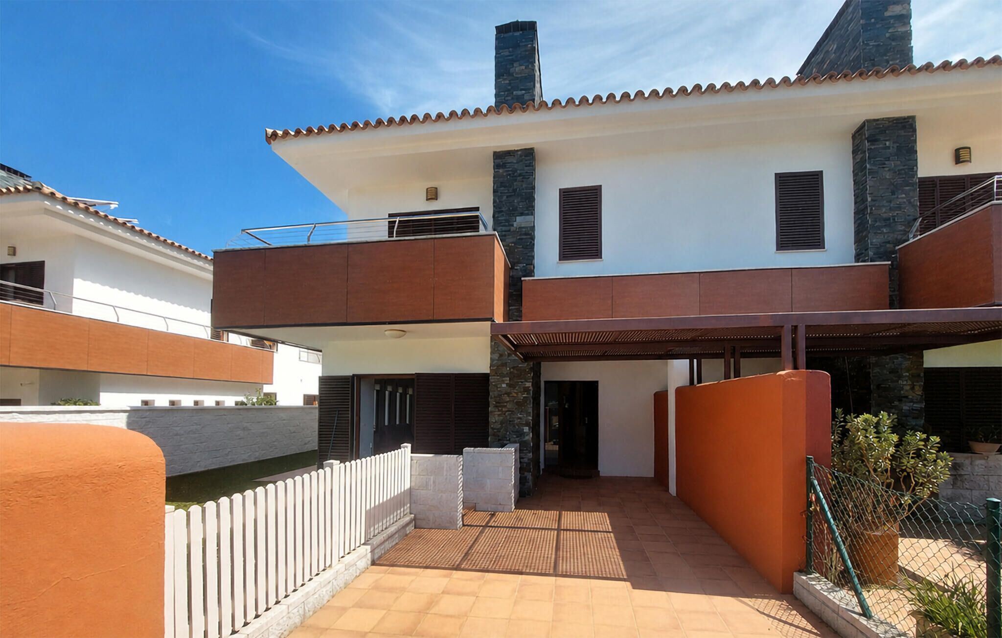 A modern two-story house with a flat roof, a covered patio, and a white picket fence.
