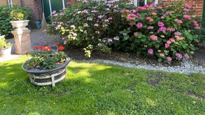 A brick building with a green door, a garden with pink flowers, and a stone planter with red flowers. - Vacation at the Horse Farm—Pets Welcome! (Jade)