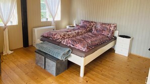 A bedroom with a wooden floor, a bed with patterned bedding, a bedside table, and a window with curtains. - Vacation at the Horse Farm—Pets Welcome! (Jade)
