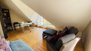 Ein Schlafzimmer im Loft-Stil mit schrägem Dach, einem Schreibtisch, einem Stuhl, einer Couch und einem Bücherregal.