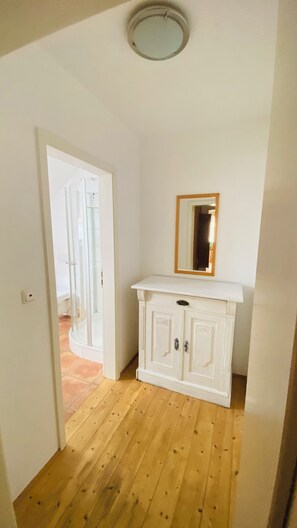 Ein Zimmer mit Holzboden, einem weißen Schrank mit zwei Türen und einem Spiegel darauf.