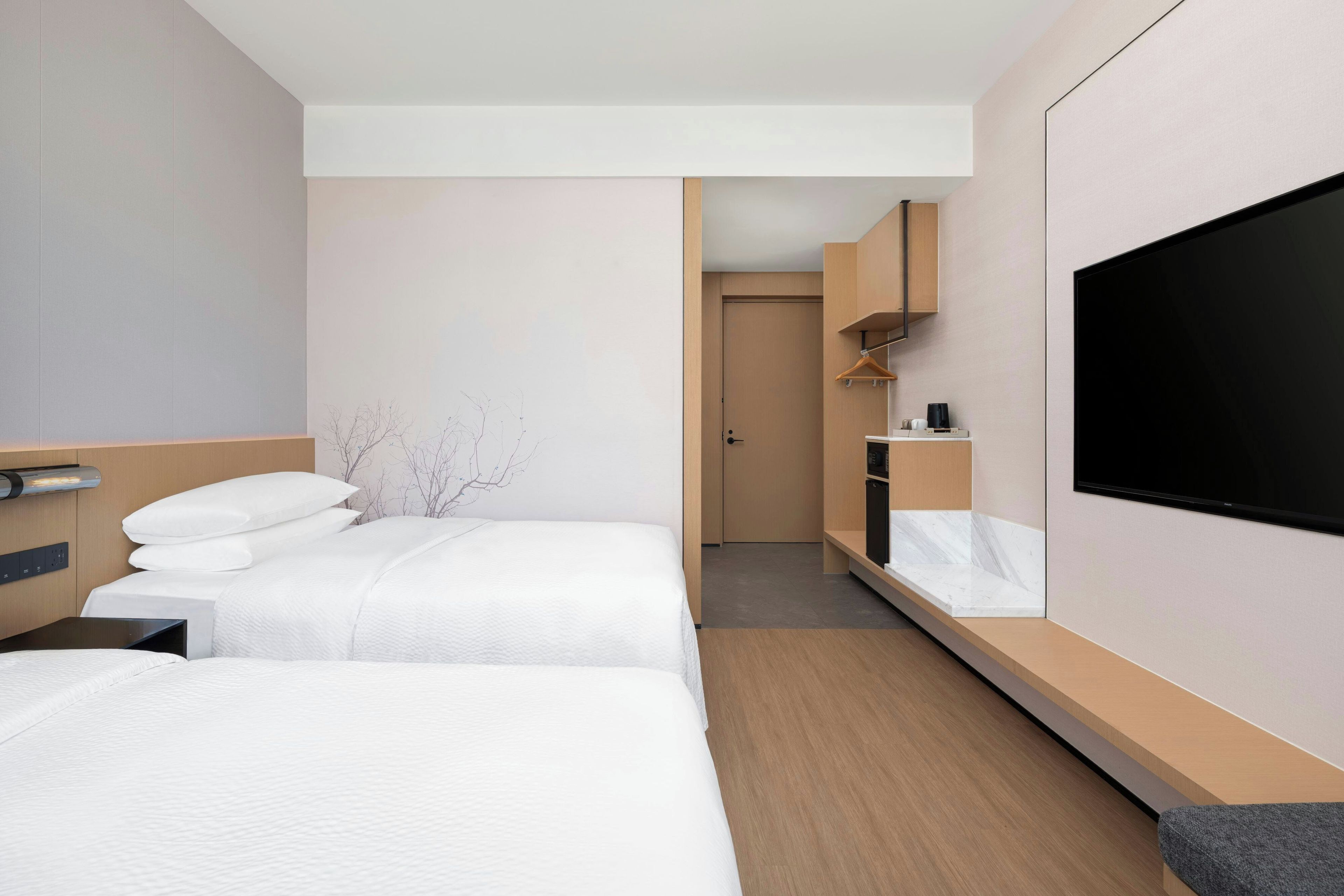 A hotel room with two beds, a TV, a minibar, and a small bathroom.