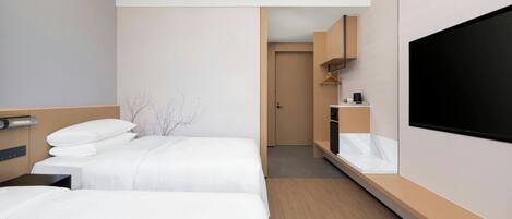 A hotel room with two beds, a TV, a minibar, and a small bathroom.