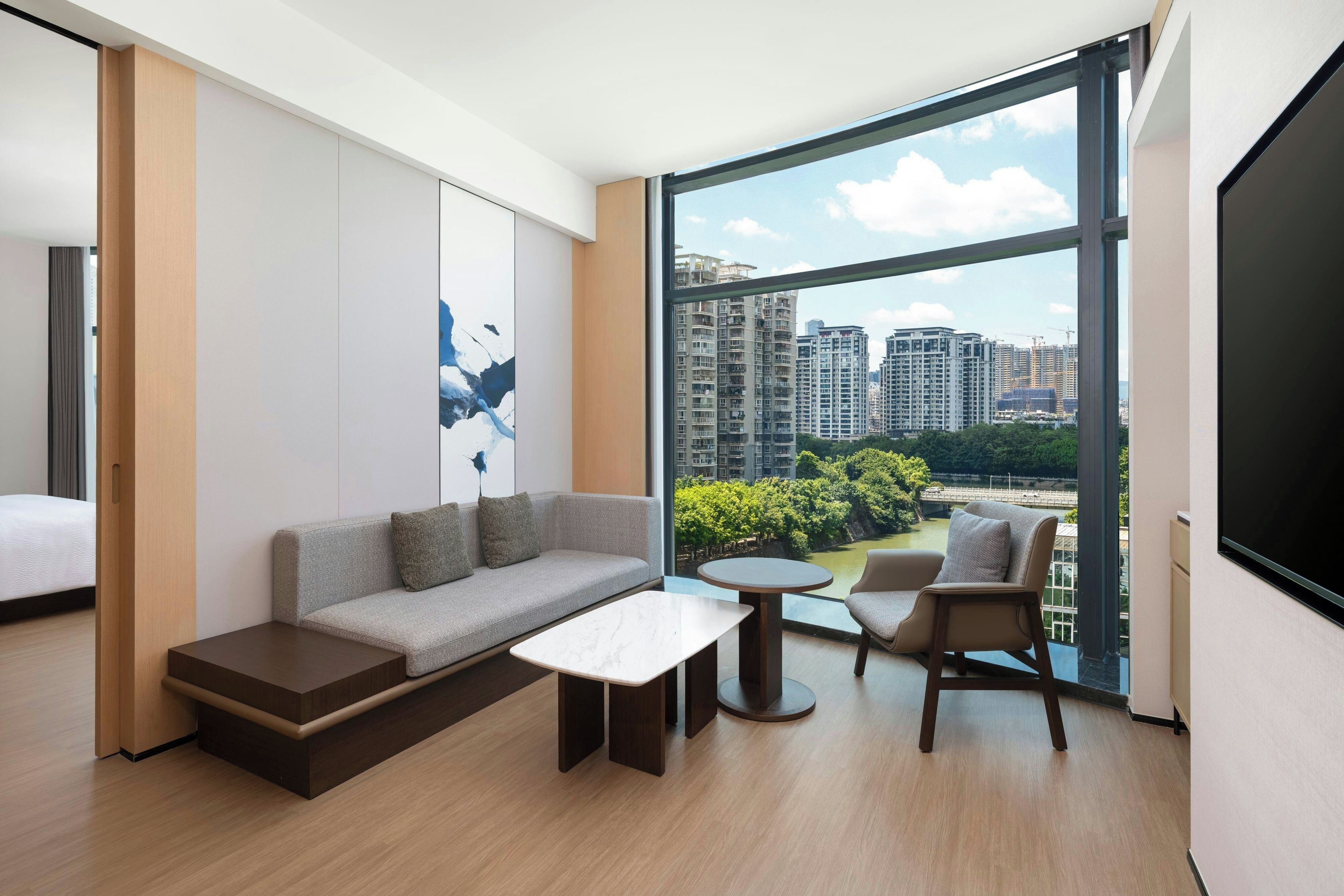 A modern hotel room with a large window, a sofa, a small table, and a chair.