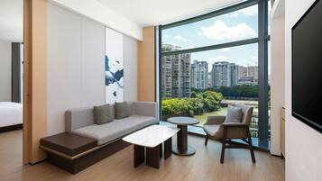 A modern hotel room with a large window, a sofa, a small table, and a chair.
