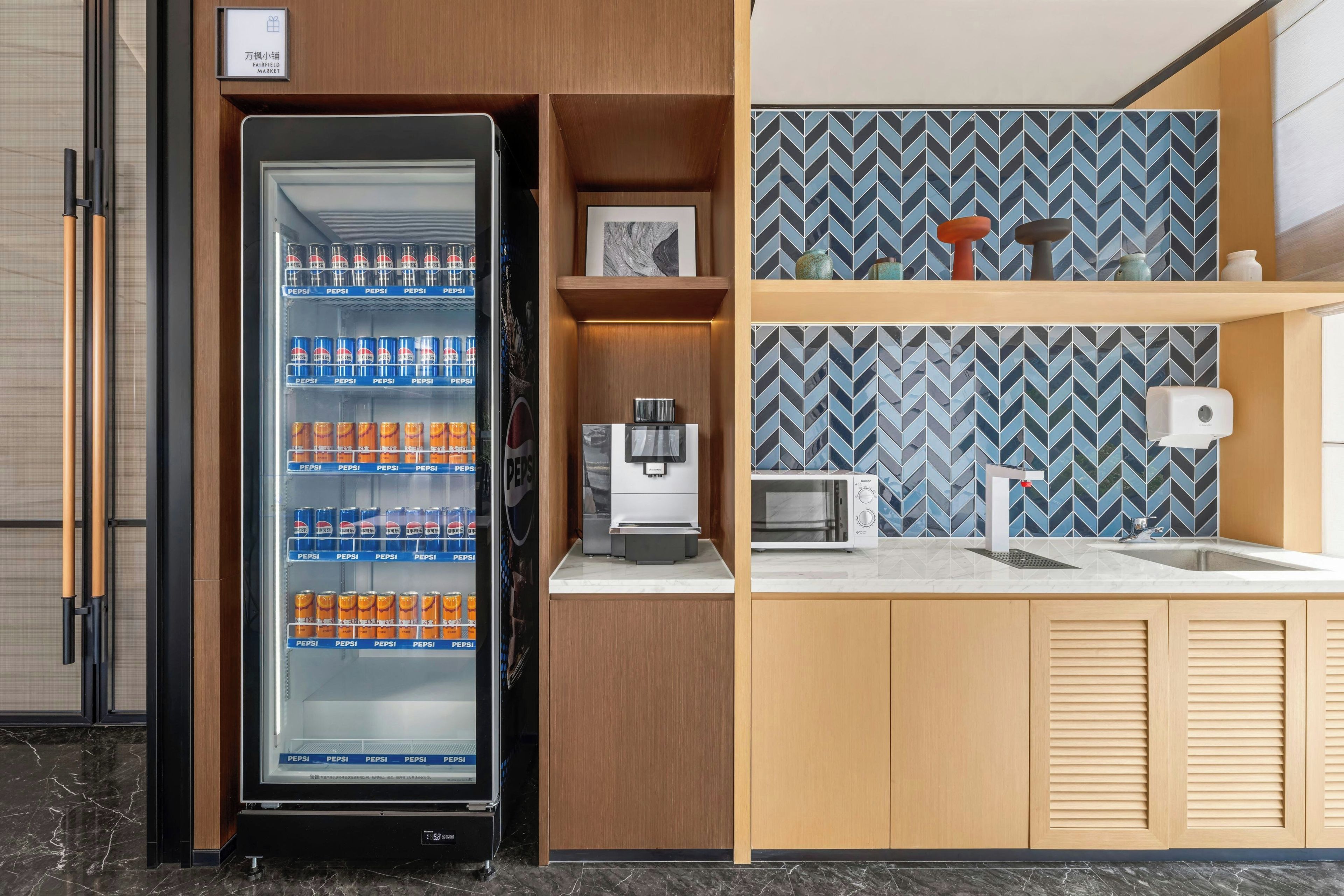A compact kitchenette with a refrigerator stocked with beverages, a microwave, a coffee maker, and a sink.