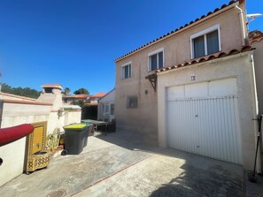Ein Wohngebäude mit Garage, Terrasse und Gartenmöbeln sowie ein kleiner Schornstein.
