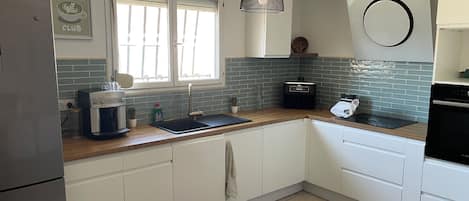 A modern kitchen with white cabinets, a coffee machine, a sink, and a window with blinds.