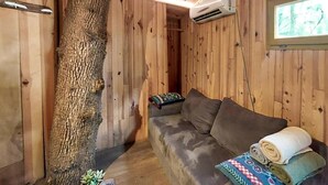 Interno di una baita in legno con un divano, un tronco d'albero e un condizionatore d'aria.