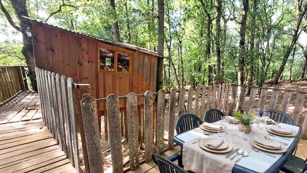 Un terrazzo in legno con un tavolo apparecchiato per mangiare, circondato da un recinto in legno e alberi.