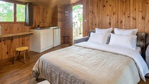 Een slaapkamer in een houten blokhut met een bed, een klein keukenhoekje en een raam.