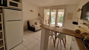 A compact kitchen with a microwave, refrigerator, and a dining area with a wooden table and chairs. - The Dune Jewel Box • Vendres-Plage • Sea & Pool (Vendres)