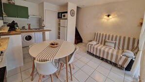 A compact living space with a dining area, kitchenette, sofa, and a staircase. - The Dune Jewel Box • Vendres-Plage • Sea & Pool (Vendres)