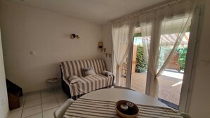 A room with a striped sofa, a dining table with a bowl, and a view through a window with curtains. - The Dune Jewel Box • Vendres-Plage • Sea & Pool (Vendres)
