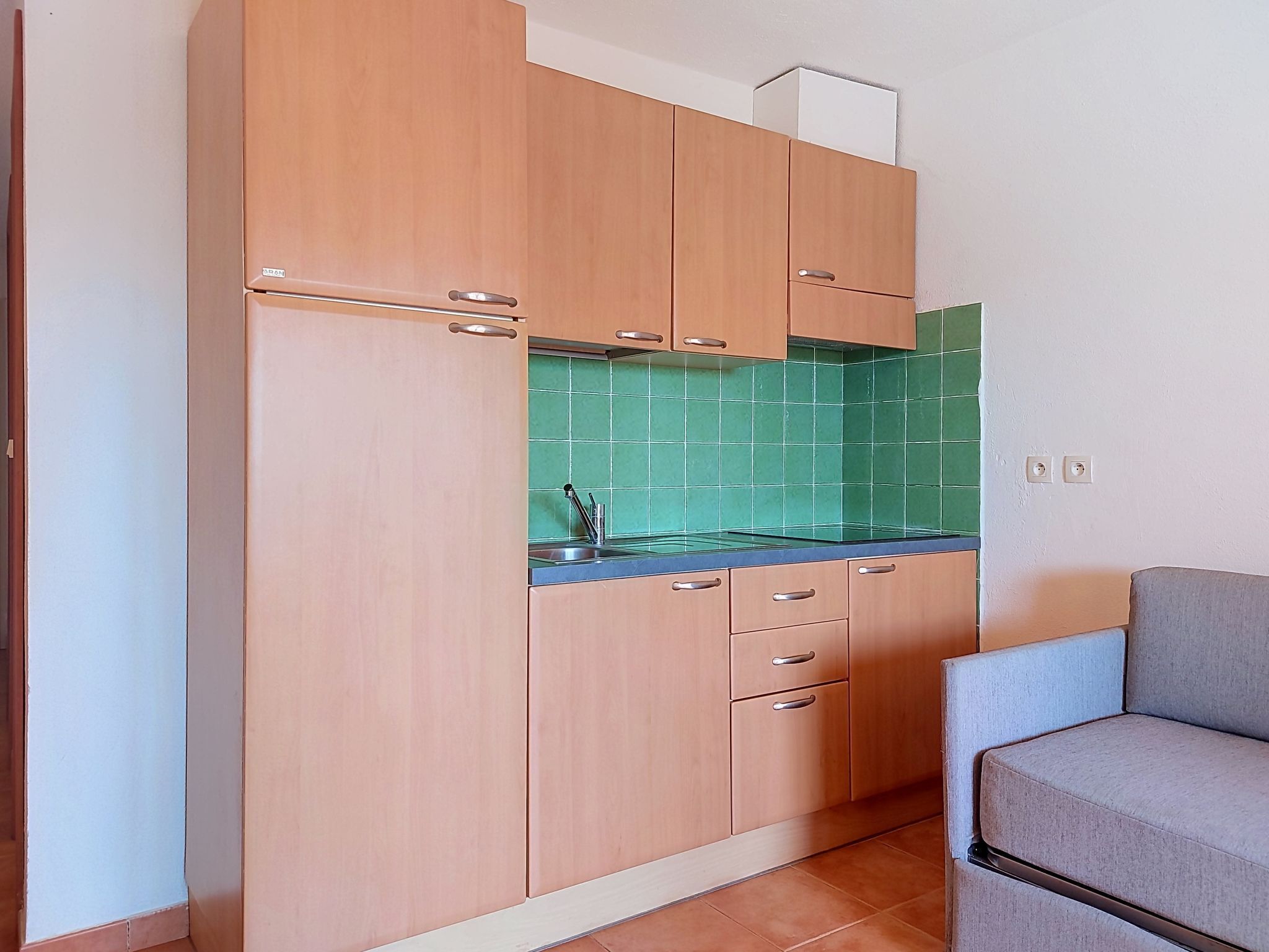 Una cucina compatta con mobili in legno, zoccolo in piastrelle e lavello incassato.