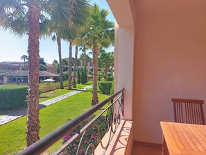 Ein Balkon mit Blick auf einen gepflegten Garten, darunter Palmen und ein gefliester Weg.