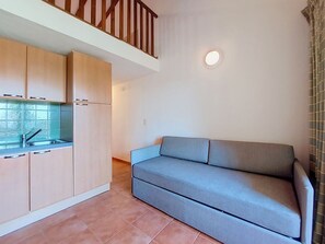 Un espai habitable petit amb una cuineta, un sofà i una escala.