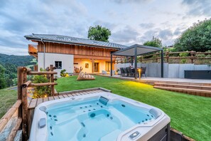 Ein modernes Haus mit Whirlpool, überdachter Terrasse und gepflegtem Rasen.