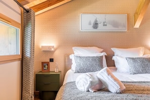 Ein Hotelzimmer mit Bett, Kissen, Nachttisch, Bilderrahmen und Wandlampe.