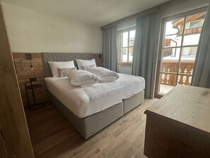 A bedroom with a bed, a bedside table, and a view of a balcony. - Chalet d'Mot, (Samnaun-Ravaisch) by Interhome (Samnaun)