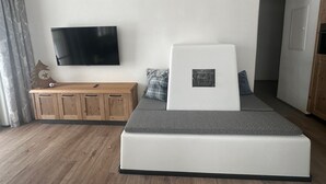 Moderni makuuhuone, jossa on sänky, seinälle asennettu televisio, puinen kaappi ja ovi, joka johtaa toiseen huoneeseen.