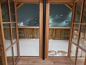 Ein Zimmer mit Holzboden, einer schwarzen Rohrleitung und Blick auf eine verschneite Landschaft durch Glastüren.