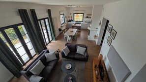 Ein geräumiger Wohnbereich mit einer Couch, einem Couchtisch und einem Esstisch mit Stühlen. Es gibt eine Küchenzeile mit einem Herd und Schränken.