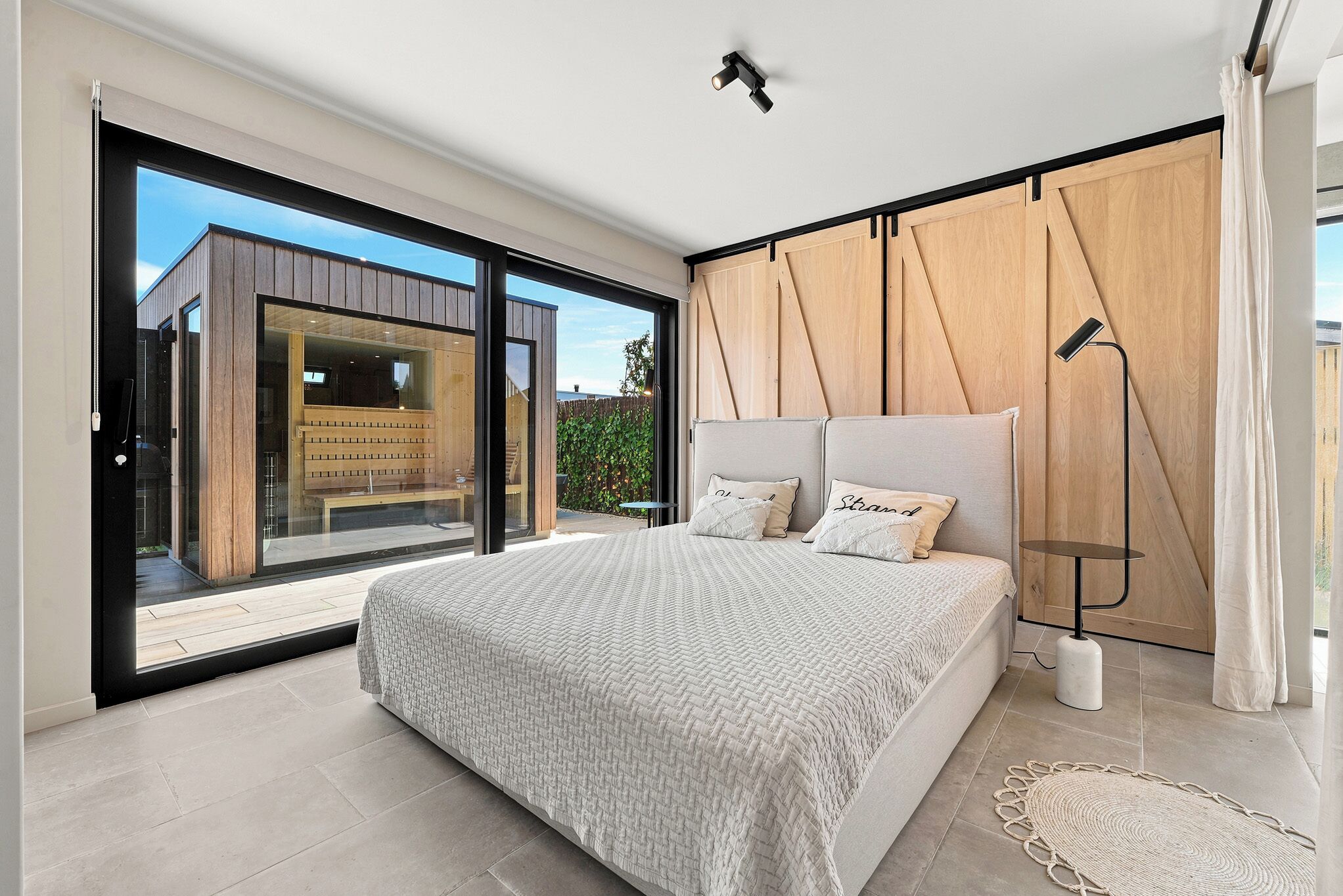 Een slaapkamer met een groot bed, een vloerlamp en uitzicht door een schuifdeur.