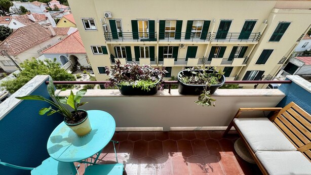 Ein Balkon mit blauem Tisch, zwei Stühlen, einer Holzbank und Kübelpflanzen.
