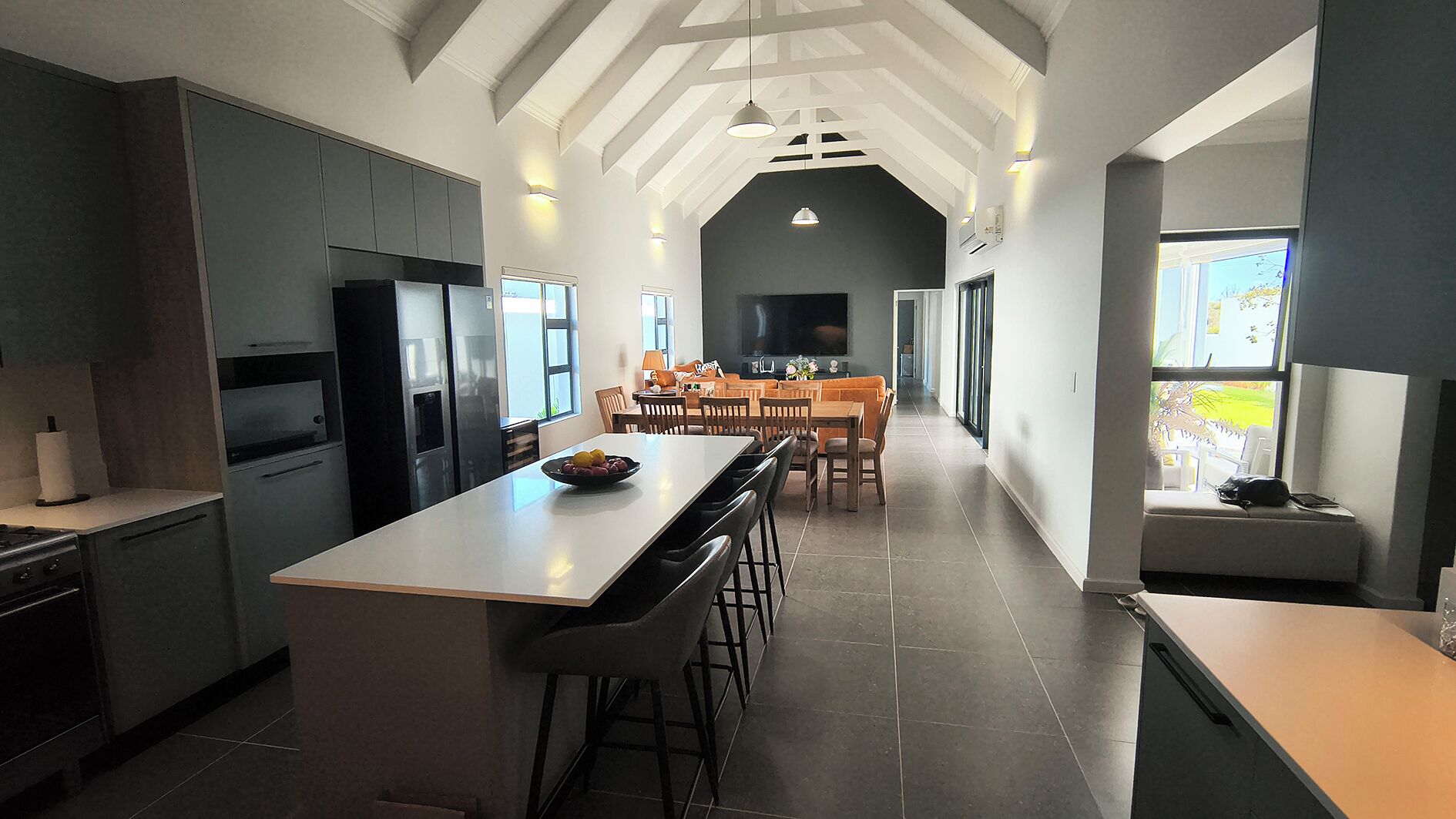 A modern kitchen with a central island, dining area with chairs, and a long hallway leading to a living space.