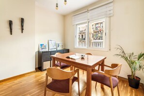 A dining area with a wooden table and chairs, a window with a view of buildings, and a potted plant. - Poble Sec Flat · 2 Balconies · A/C · 4 Guests · Near Montjuïc (Barcelona)