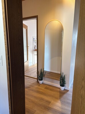 A hallway with wooden flooring, a large mirror, and two potted plants. - View of the Staffelstein Mountains & A Balcony Dream – 60-square-meter vacation rental in Bad Staffelstein (Bad Staffelstein)