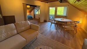 Ein gemütliches Zimmer mit einer Couch, einem Esstisch mit Stühlen, einem Fenster mit Aussicht und einer Holzzieldecke.