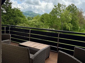 A balcony with wicker furniture and a view of a green landscape. - View of the Staffelstein Mountains & A Balcony Dream – 60-square-meter vacation rental in Bad Staffelstein (Bad Staffelstein)