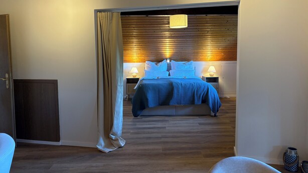 Ein Schlafzimmer mit einem Bett, Nachttischlampen, einer Holzbalkendecke und einer Tür.