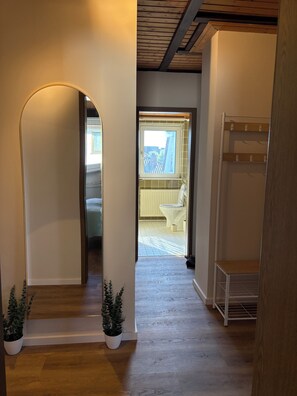 A hallway with a wooden floor, white walls, and a skylight. There are two potted plants and a white metal rack. - View of the Staffelstein Mountains & A Balcony Dream – 60-square-meter vacation rental in Bad Staffelstein (Bad Staffelstein)